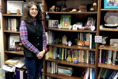 一位女教授站在摆满书的书柜前, 照片, 还有不同的纪念品 