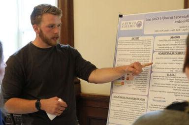 在学生研究会议期间，一名男学生在海报板上参考他研究中的要点